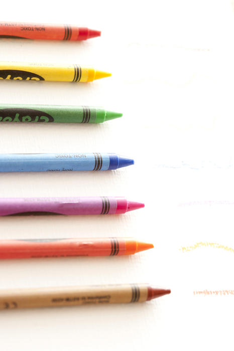Row of colorful new kids wax crayons arranged in a receding line over white with copy space for education and art concepts