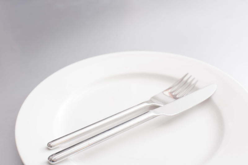 Empty clean generic white plate and silver cutlery with a knife and fork neatly arranged in the centre in a cropped view