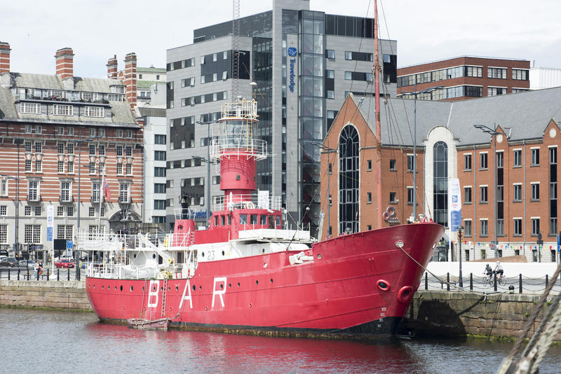 Converted colorful red ship bar moored to the quay at Liverpool waterfront, UK, in front of historic listed buildings in a travel and tourism concept
