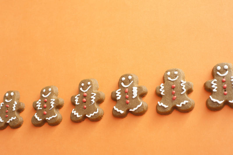 Slanted row of gingerbread men cookies with white and red icing over orange background