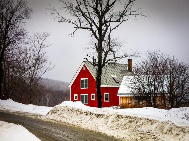 <p>Little red Christmas House and barn in the winter by the road with snow and naked trees, rural Vermont.</p>
