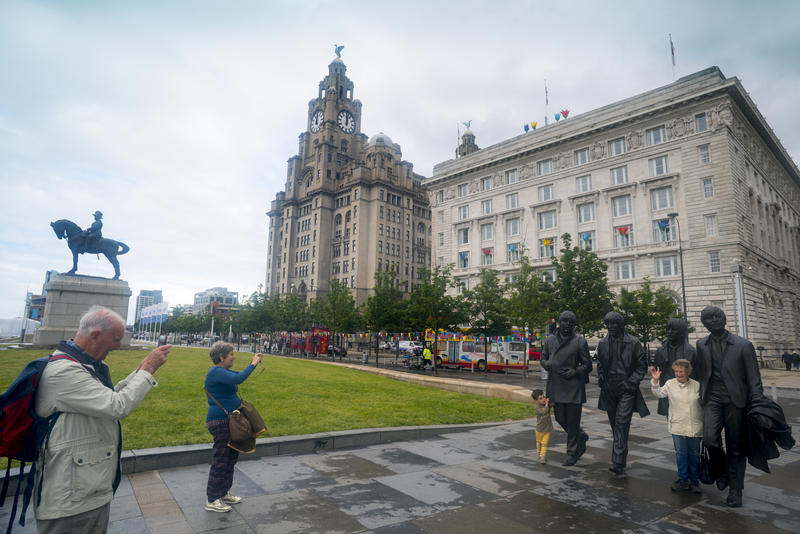 Tourists taking photographs at the Beatles statue in Liverpool, UK with the historic Live Building in the background