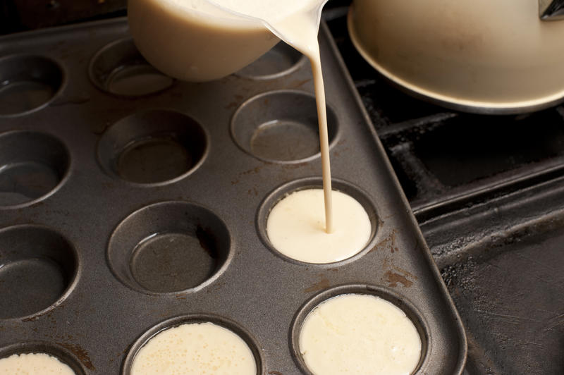 Cook pouring freshly made batter from a jug into a baking tray with individual cup holders for a batch of English Yorkshire puddings