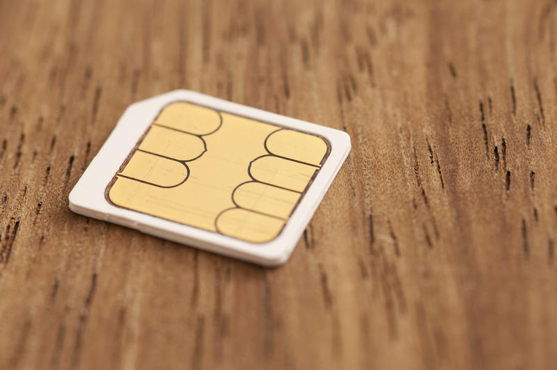 White micro sim card with chip side up in close-up macro image on wooden surface background. Copy space