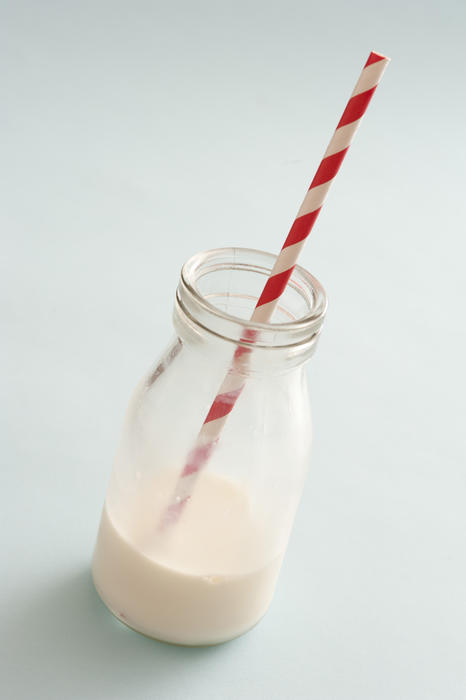 Creamy milk fills bottom of short glass bottle with stripped straw against a light colored background
