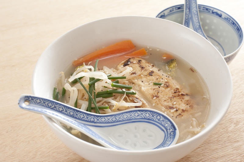Spoon on side of bowl of delicious soup broth with milkfish chunks, seasoning, chives, carrots and noodles