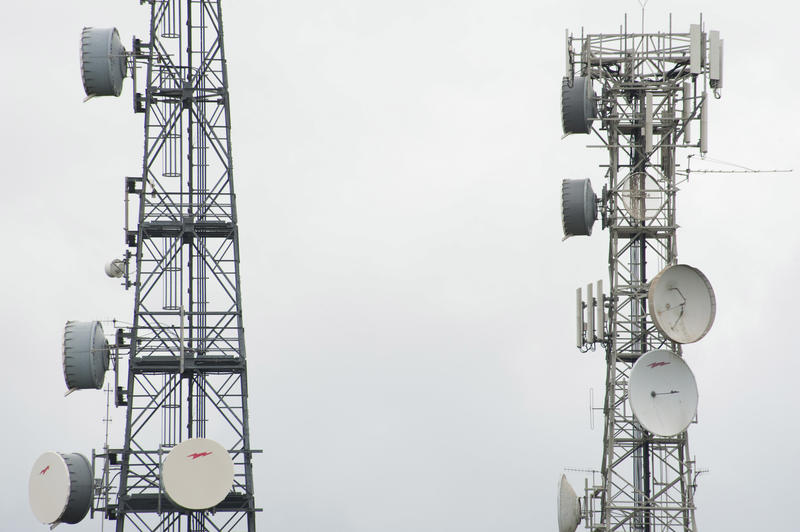 Two telecommunications towers with transmitters and receivers for mobile phones on a grey cloudy day