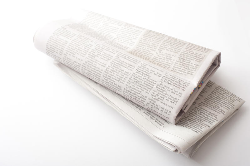 Folded newspapers with black ink text over neutral color background for concept about news