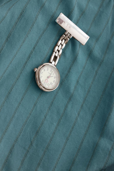 Nurses silver fob watch with a blank name tag pinned on a uniform in a close up view with copy space