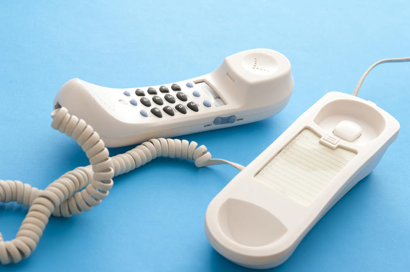 Land line telephone lying off the hook with the handset alongside the base and twisted cord on a blue background in a communication concept
