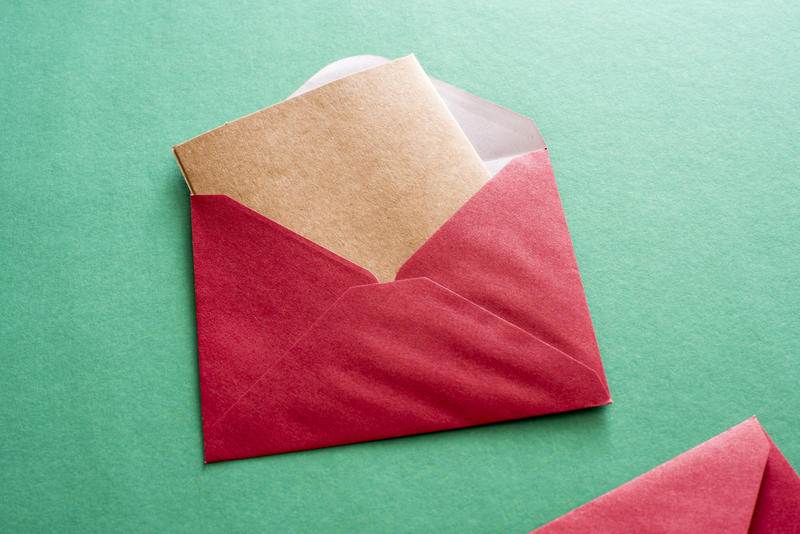 Blank brown card in a red Christmas envelope protruding from the opened flap over a green background with copy space