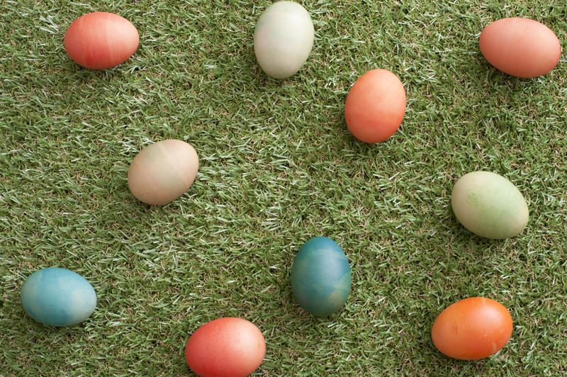 Scattered homemade multicolored dyed Easter eggs on neat short fresh green grass viewed from above in a festive background