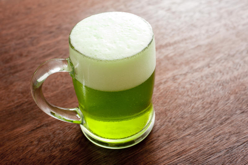 Single glass mug full of beer with green coloring and white foam on top above wooden table
