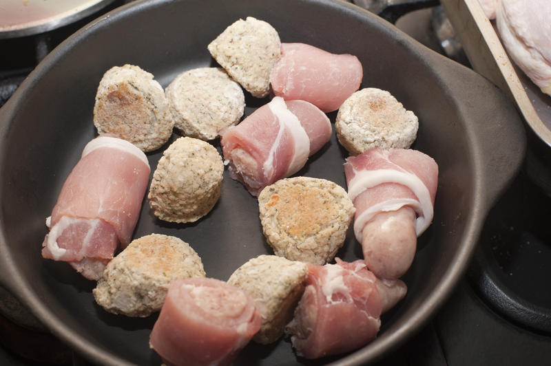 Pigs in blankets, or bacon rashers wrapped around pork sausages, ready for cooking in a pan, close up high angle view