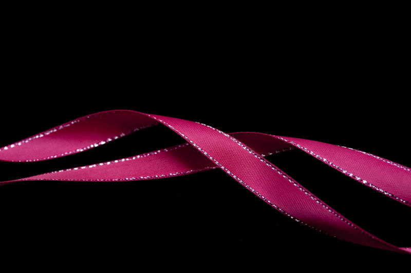 Two twirled festive pink ribbons forming a line across a dark background with copy space