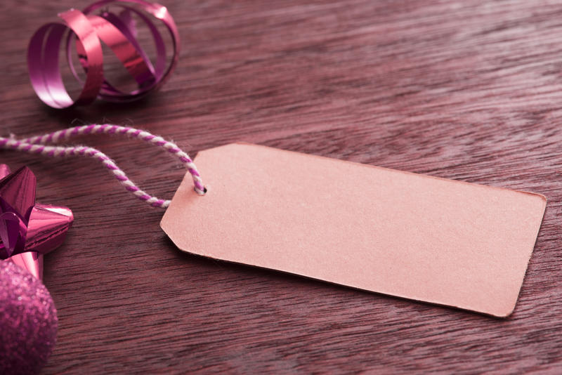 Blank gift tag with Christmas packaging items such as a red twirled ribbon and spiky bow forming a side border on textured wood
