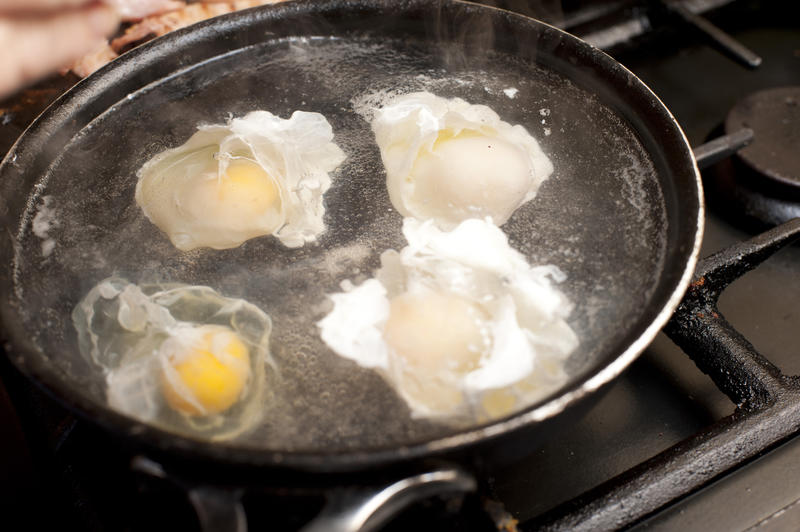 Four poached eggs nearly fully cooked in pot of boiling water on gas stove top