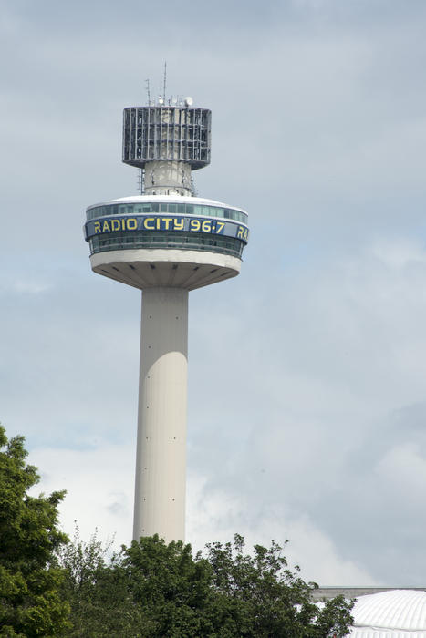 View of the Liverpool Radio City Tower rising above foliage against a grey cloudy sky in a travel and communications concept