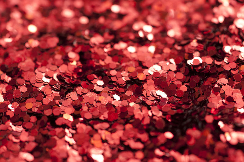 Background texture of sparkling red glitter in a close up macro view with shallow DOF for a festive or craft concept