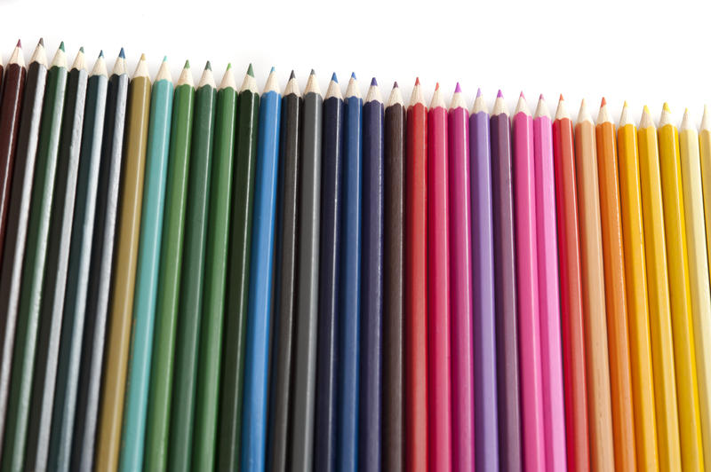 Row of sharp new blue, green, red and orange colored pencils arranged diagonally over white background