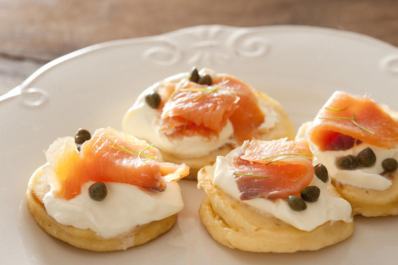 Close up on four salmon caper blinis with cream cheese and capers on white plate