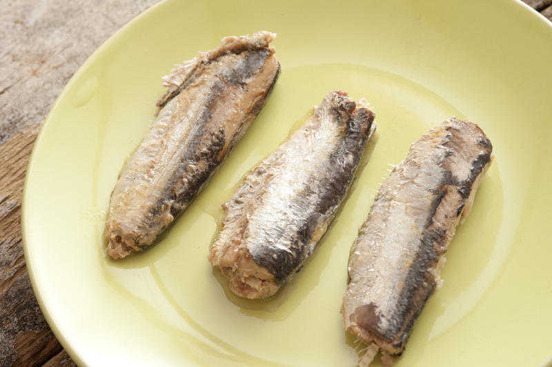 Three ready to eat sardines without head or tail on yellow circular plate over wooden surface