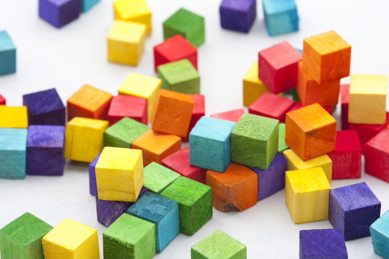 Scattered piles of green, yellow, purple, blue and orange cubed play blocks on gray background