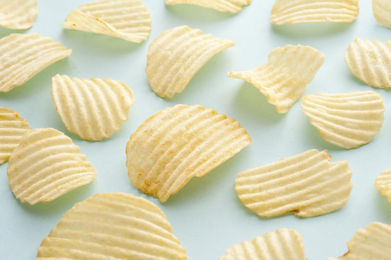 Group of separate full sized crispy ridged potato chips as background about snack food over blue