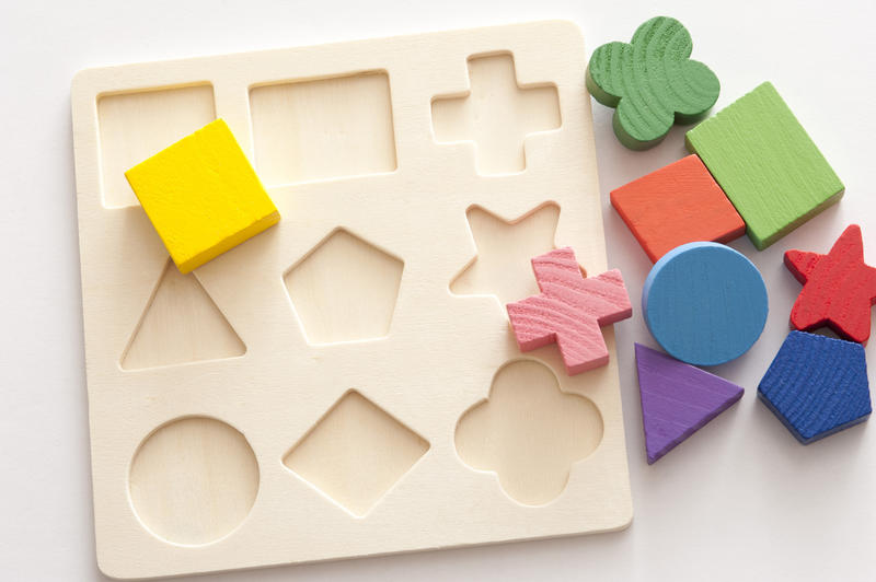 Educational kids shape puzzle with cutouts for matching basic geometric shapes in colorful wood, high angle view