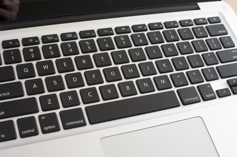 High angle close up view of an open silver laptop showing the touch pad and keyboard with black keys