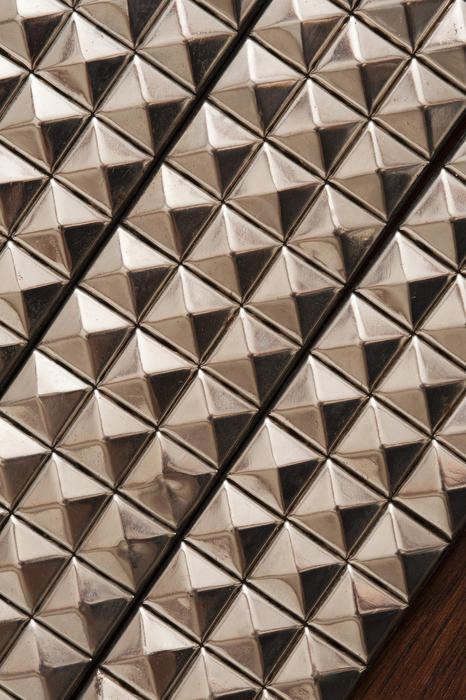 Background texture of pyramidal silver studs in a repeat pattern with oblique lighting enhancing the shape