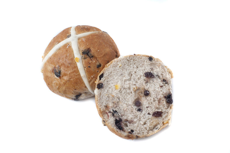 Close up view of sliced hot cross bun with raisins, and one whole bun marked with white cross, isolated on white background