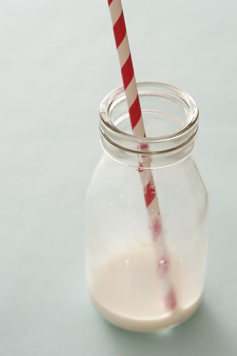 Small empty milk bottle with a colorful red striped straw and the remnants of the consumed drink in the bottom, close up high angle conceptual of a healthy diet for kids
