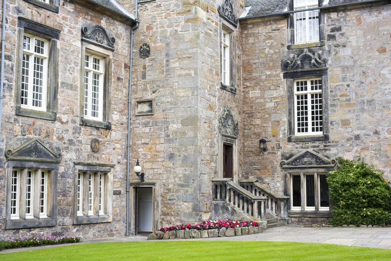 View across a manicured lawn to entrance stairs to one of the historic stone buildings at St Andrews University, Scotland