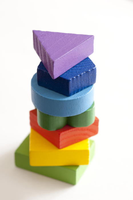 Stack of colorful wooden toy bricks in the colors of the rainbow in basic shapes including a circle, triangle, square and pentagon viewed close up high angle on white with copy space
