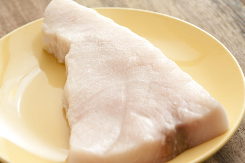 Close up of on chunky cut of swordfish in round yellow plate placed on rustic wooden table