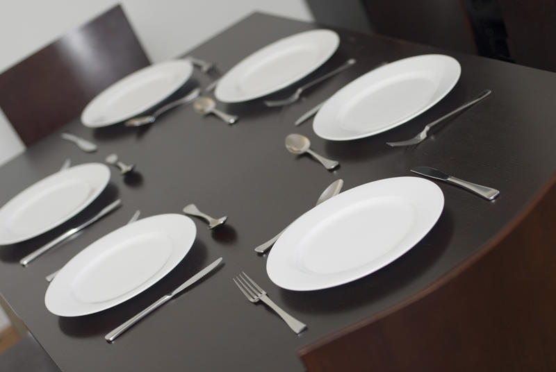 Dinner table laid for a family meal with cutlery and generic white dinnerware viewed at a tilted angle