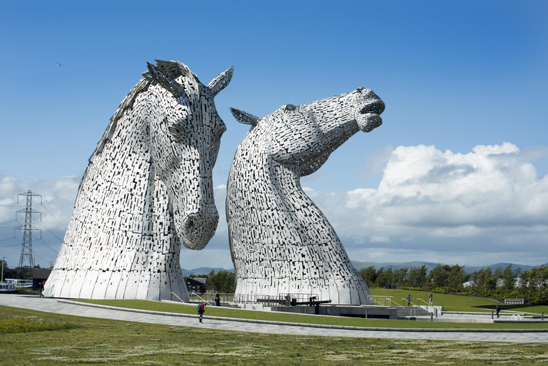 Small people walking along paths past the Kelpies statues in Falkirk Scotland