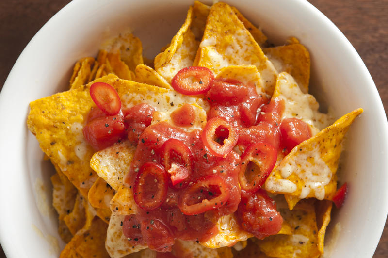 Savory yellow tortilla chips covered in peppers and melted cheese as seen from an overhead view