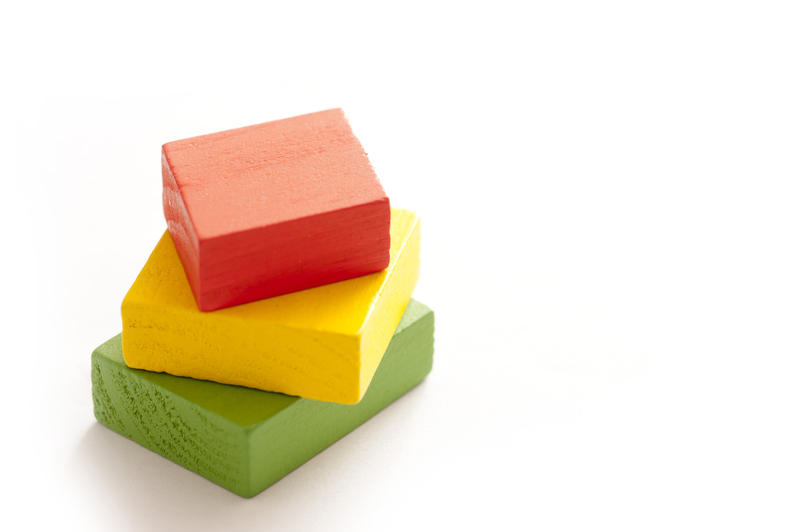 Three educational wooden toy blocks in different sizes and colors - red, green and yellow - stacked on top of one another on a white background with copy space