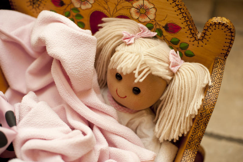 High Angle View of Doll with Blond Hair Nestled Under Pink Blankets in Handmade Wooden Cradle in Family Home