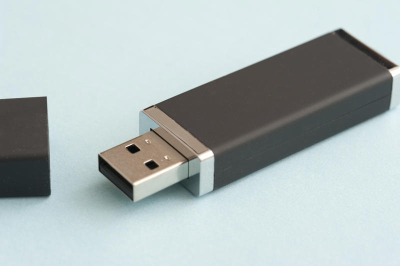 Single black USB drive or memory stick for a computer lying on a light blue background with the cap off
