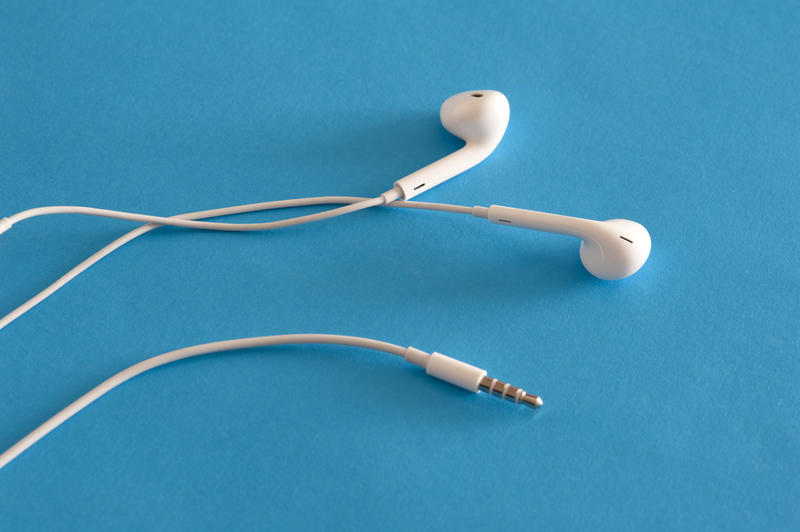 White earbuds with mini jack for audio and sound lying on a blue background with copy space