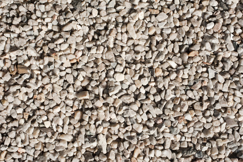 Close up overhead view of light colored gravel illuminated by a bright afternoon sun