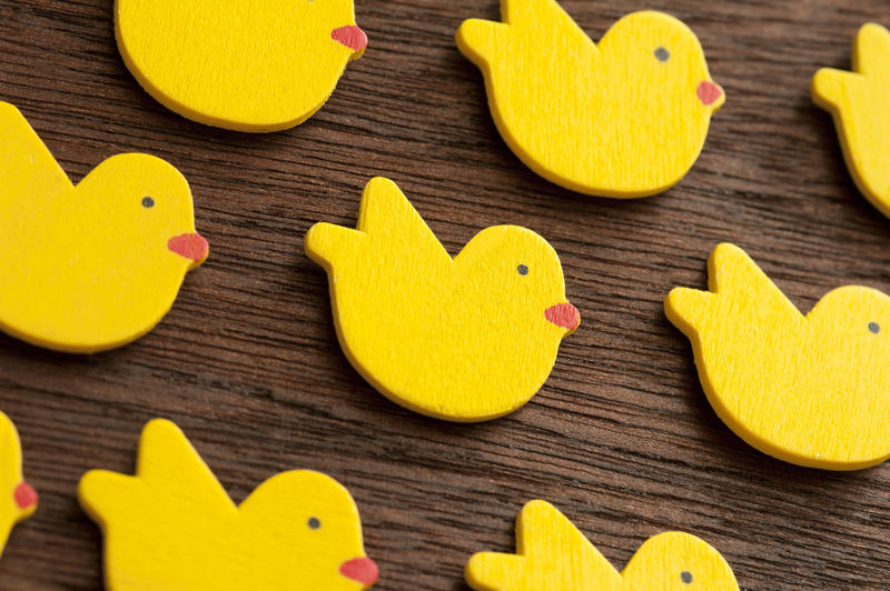 Rows of yellow wooden shapes of small Easter chicks decorations or toys over lacquered table surface background