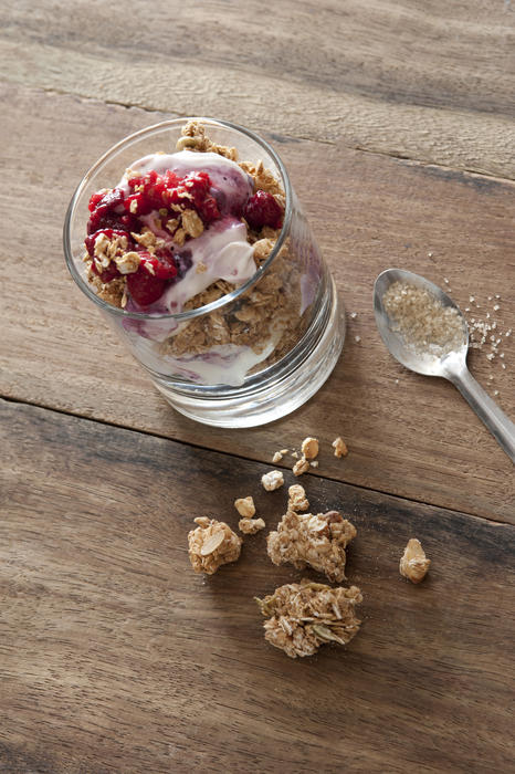 First person perspective view on single glass full of muesli cereal, yogurt and fruit on wooden table and spoon with wheat germ