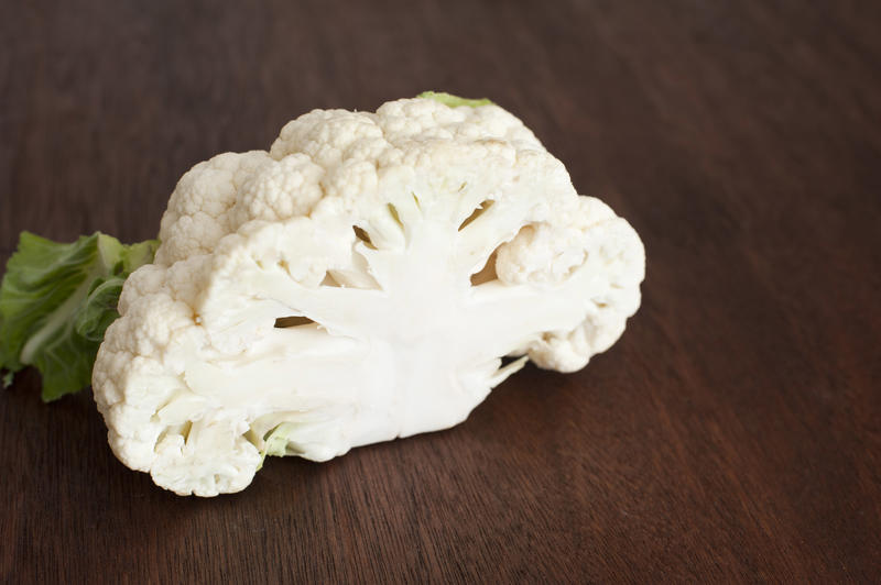 A close up of a halved cauliflower head on a timber bench.