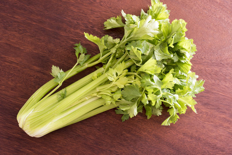 A bunch of fresh green celery in close-up on brown wooden surface, viewed from above