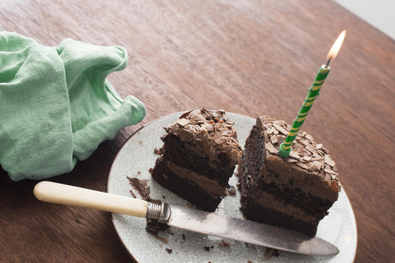 Remnants of a chocolate birthday cake with green candle on a plate with a knife viewed high angle on a table