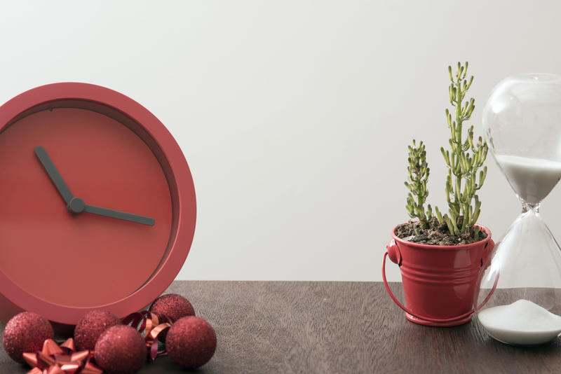 Christmas countdown wit festive red clock surrounded by decorations on a wooden table with hourglass